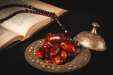 Dried dates with an open Muslim holy book Quran. Muslim holiday of the holy month of Ramadan Karim on a dark background