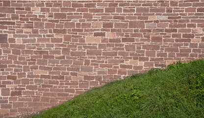 Alte Mauer aus rotem Sandstein hinter einem grünen Grashügel