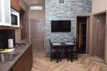 Dining room with TV above the dining table. Interior of a modern kitchen. Kitchen in brown tones with a wall imitating a brick. Interior of the cottage. Guest house from the inside.