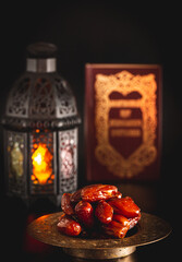 Dried dates with an open Muslim holy book Quran. The Muslim holiday of the holy month of Ramadan Karim on a dark background. Beautiful background with shining Fanuc lantern
