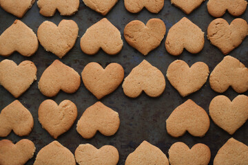 Raw cookies in the shape of hearts are cut out of the test mold and is in the baking tray with empty space. Top view, horizontal