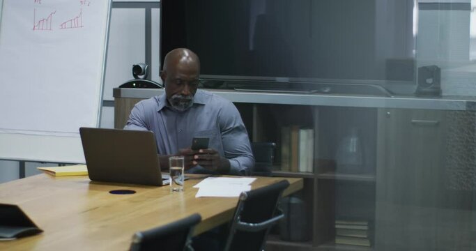 African american businessman using smartphone and laptop in conference room at office