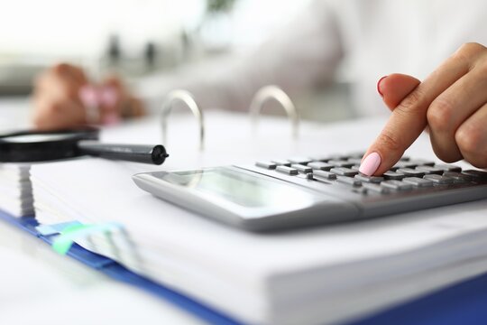 Woman counting on calculator at table with documents closeup