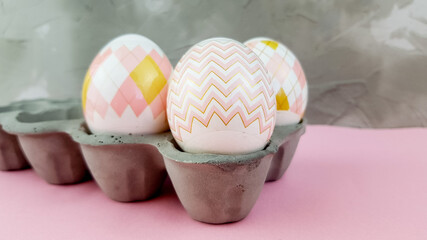 eggs of a delicate color in a concrete egg box on a plastered background on a pink table. an interesting combination of colors and textures.