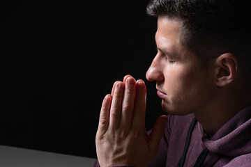 A man prays. The man closed his eyes and folded his hands in front of his chest. The concept of religion and faith. The guy prays to God. Believing man.