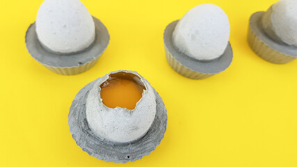 Fototapeta na wymiar egg made of concrete with a yellow yolk of gray color on a lemon background