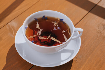 White cup of herbal tea with a saucer. Bright sunlight. The concept of tea drinking, healthy drinks.