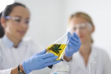 Woman chemist holding flask with yellow liquid marijuana closeup