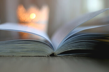 Open book and lit candle on a table. Selective focus.