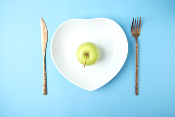apple, cutlery and empty plate on blue background top down
