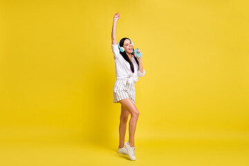 Fototapeta na wymiar Full size photo of young pretty lovely cheerful smiling gin singing in headphones isolated on yellow color background