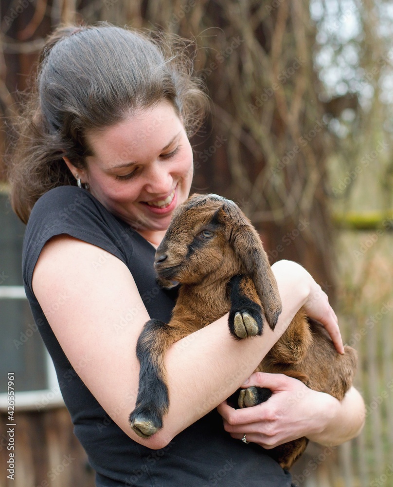 Sticker young woman farmer with adorable baby goat in the arms (capra aegagrus hircus)