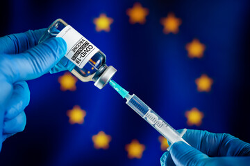Injecting dose of vaccine in syringe for Covid-19 over the European flag. Doctor preparing vial of...