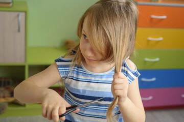 a cute little girl cuts her hair with scissors.