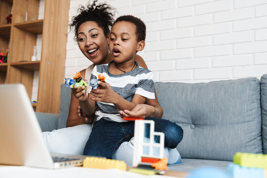 Black happy woman using laptop while playing with her son at home