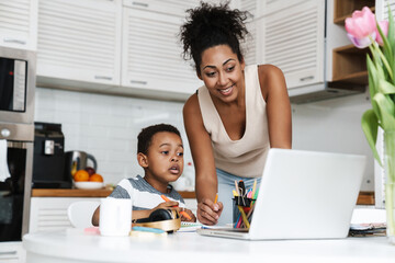 Black mother using laptop while doing homework with her son at home