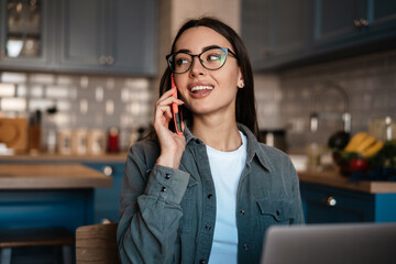 White smiling woman talking on cellphone while working with laptop