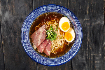 Japanese ramen noodle soup with pastrami and eggs on the wooden table