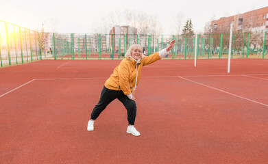 Fototapeta premium an elderly woman in a yellow jacket is doing sports exercises on a red treadmill. the stadium is a healthy lifestyle. retired people and sports.