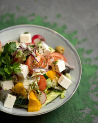 Salad with Fresh vegetables and cheese. Vitamin Mix of tomato, radish, cucumber, olives, greens and feta. Holiday or festive dish, nicely served food plate on restaurant table. Soft focus. Close up.