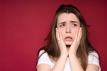 Sad young girl in a white T-shirt suffers from pain in the oral cavity touching her face with her...