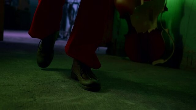 Close-up of the shoes of a clown in a broken room goes to the camera. Green light fills the room