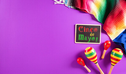 Cinco de Mayo holiday background made from maracas, mexican blanket stripes or poncho serape on purple background with the text.
