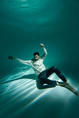 Obraz premium Arabian man in formal wear sitting on bottom of swimming pool