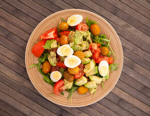 dish of fresh vegetables arugula, avocado, cherry tomatoes with olives and quail eggs on dining table