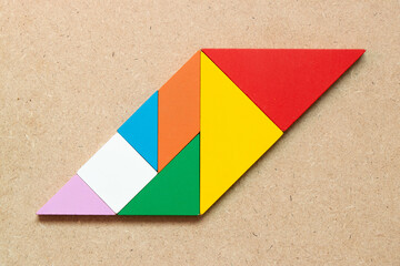 Color tangram puzzle in parallelogram shape on wood background