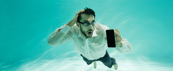 Astonished muslim businessman holding cellphone while swimming in pool, banner