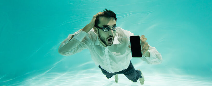 Astonished muslim businessman holding cellphone while swimming in pool, banner