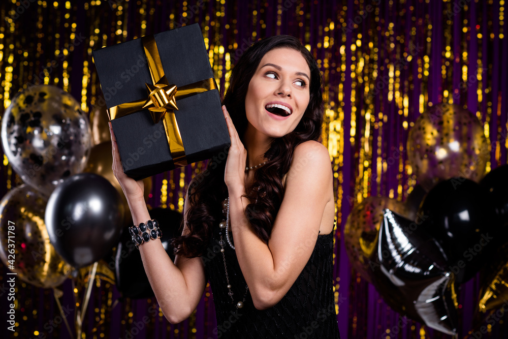 Sticker Portrait of gorgeous positive lady arms hold giftbox near head look empty space isolated on shiny curtain background