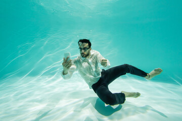 Arabian businessman in goggles looking at cellphone in swimming pool