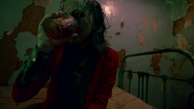 A person with a clown makeup in the room drinks alcohol in a state of depression