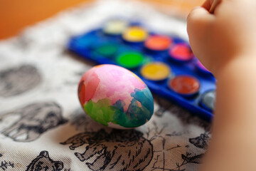 Hand-painted Easter egg and watercolors close-up. Toddler holding paintbrush while painting egg.