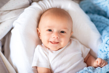 Cute newborn baby boy in white body laying in his cradle with soft blue blanket.