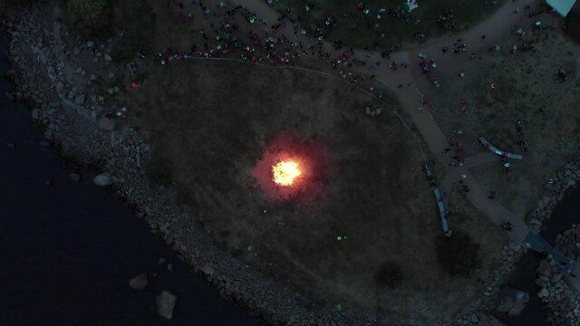 Bonefire midsummer nearby the sea surrounded by people Helsink, Kotka Finland top view. drone high angle birds eye movement. beautiful sunset people enjoy the warm weather