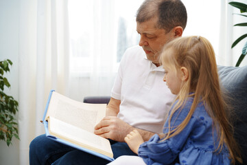 Grandfather reading a book to his little graddaughter in living room