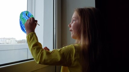 Cute little girl painting planet on window at home 4K. Happy Earth Day April 22 greeting message. Creative family leisure lockdown new reality. Ecology Saving environment conscious consumption concept