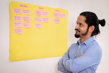 Business young man working on a scrum planning made on a yellow board on a white wall. Young man...