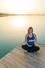 Portrait of a young happy pregnant woman on a jetty during a beautiful sunset