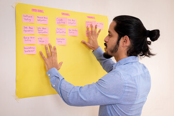 Business young man working on a scrum planning made on a yellow board on a white wall. Young man working on a project