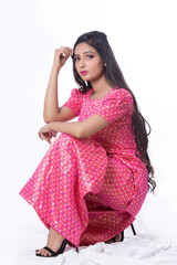 Young Indian girl posing in a studio in a siiting pose for a model shoot wearing pecil hill shoes and  a pink coloured  traditional and ethnic dress called sharara