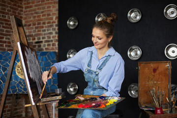 Young beautiful female artist painting still life with sunflower on canvas using oil paintings and art brush. Painter creating artwork in art studio. Relaxation, leisure, hobby, stress management