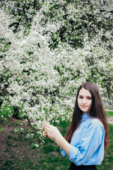 A pretty brown-haired girl poses near a flowering tree. White flowers on a tree. Garden cherry