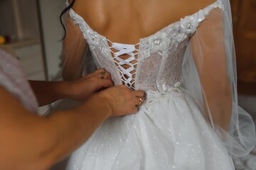 Bridal morning, bride wears dress. Groom helping fiancee to get dressed, adjusting buttons on wedding gown, rear view. close-up, crop