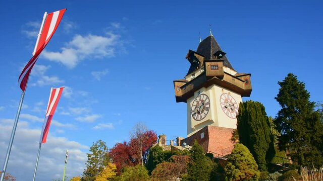 The famous clock tower on Schlossberg hill, one of the city of Graz attractions and the national flag of Austria waving in the wind, in Styria region, Austria