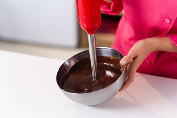 A red blender mixes liquid dark chocolate. chef hands, no face