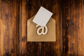 An email sign with white blank paper on a craft envelope lies on a vintage wooden table. Concept e-mail message letter. Top view with copy space